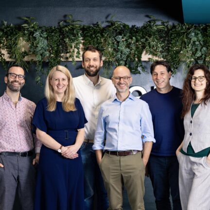 Riverlane leadership team standing together smiling for a photo in their office. From left to right is Earl Campbell, VP Quantum Science, Rebecca Simmons, Chief Operating Officer, Marco Ghibaudi, VP Engineering, Steve Brierley, Founder & CEO, Glenn Manoff, Chief Marketing Officer, Maria Maragkou, VP Product & Partnerships.